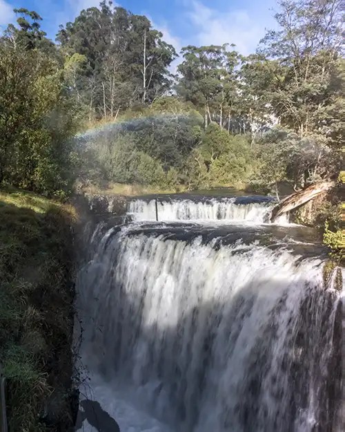 There is a rainbow in the mist above Guide Falls waterfall.
